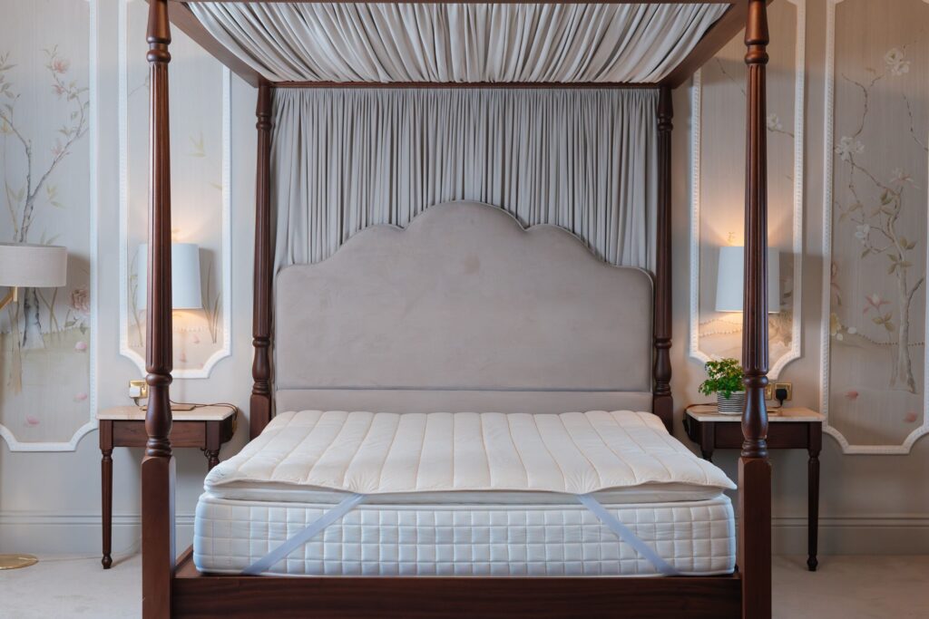 A neat bedframe in a grandiose room with a mattress and a wool mattress topper from Dooley's Wool on top of it